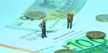 Illustration, 2 verkleinerte Männer stehen auf Geldscheinen und einer Einkommensteuer-Erklärung